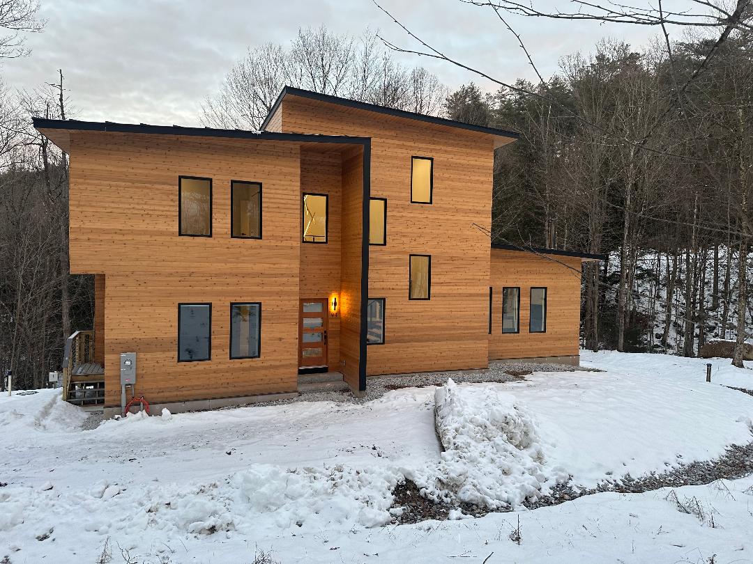 Modern wooden house with warm interior lights in a snowy landscape.